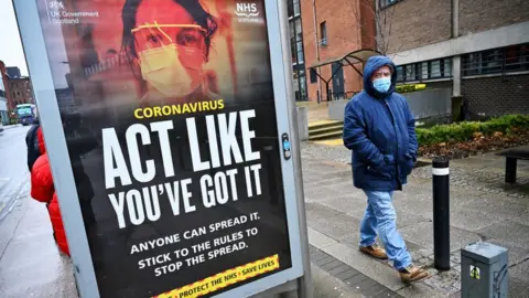 Getty Images Members of the public walk past a government poster reminding people to socially distance and abide by the lockdown restrictions in the city centre on January 29 2021 in Glasgow