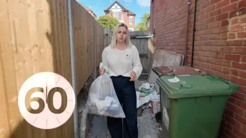 A woman with blonde hair holding a bin bag 