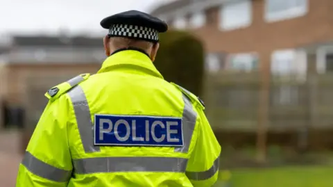 Getty Images A police officer standing with his back to the camera. He is wearing a his-vis jacket with the word POLICE written on it.