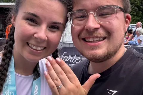 Sarah John Sarah holding her hand up with an engagement ring beside Thomas, both smiling