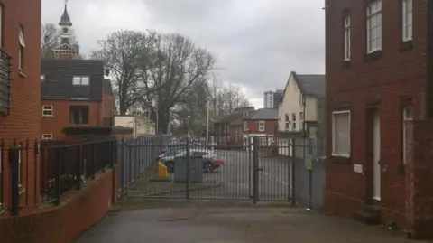 The entrance gates to Lincolnshire Archives, with buildings on either side and cars parked in the distance