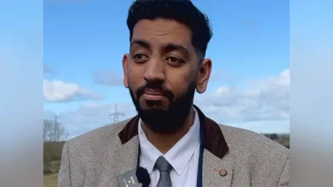 Councillor Armaan Khan stood in front of a green field.