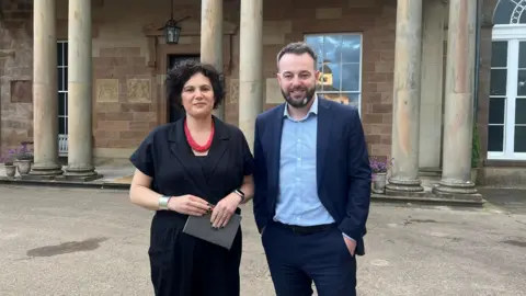 SDLP MPs Colum Eastwood and Claire Hanna stand outside Hillsborough Castle