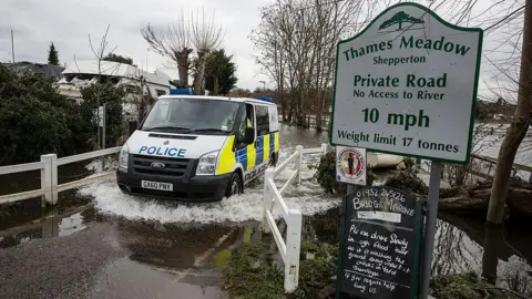 A police van driving through a flooded area in Thames Meadow, Shepperton