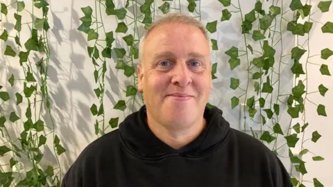 One of the directors of the cafe, Jason Baker, wearing a black hoodie and smiling into the camera.