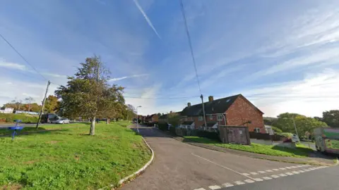 Entrance to Salterton Road, Exmouth. There is an area of grassland to the left with terrace housing on the right. 