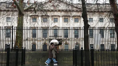 Reuters A woman holding an umbrella past black railings in front of the Royal Mint Court, the proposed site of the new Chinese embassy in London.