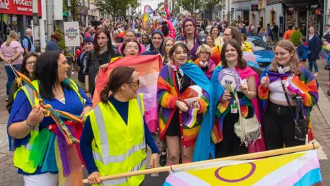 A crowd of people dressed in rainbow colors and holding flags celebrate the Pride festival in Omagh.