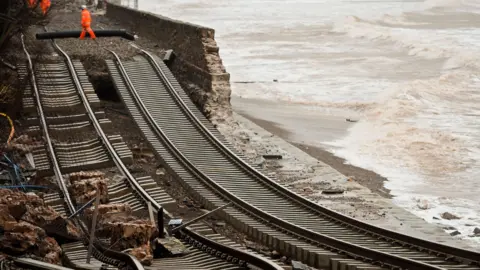 PA Media A picture of the damage caused during a storm in 2014. The railway line is pictured and completely collapsed. There is workers in hi-visibility in the distance.