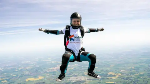 Maddy Warren A woman grins as she skydives, wearing a white Kidney Care UK T-shirt.