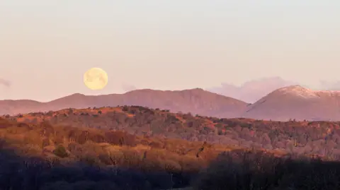 BBC Weather Watchers/lilebeck The large full moon rises in the pink sky above mountain peaks in Cumbria.