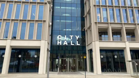 LDRS The outside of Sunderland City Hall which is a large building with large rectangle windows with 'City Hall' written in large white letters above the glass entrance.