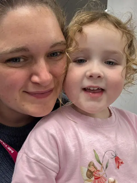 Family handout. A mother and young daughter are pictured together smiling into the camera for a selfie. The mum has a dark jumper on while the girl is wearing a pink top and has curls in her hair. 