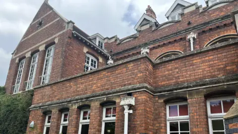 A photo of a school building with redbrick walls and a number of white framed windows