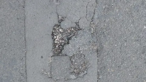 A picture from above of a pot hole on a tarmac pavement.