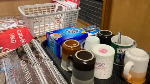 A tray of coffee mugs can be seen on the right. One has a spoon in it suggesting it has been used. There is also a box of tea bags. These have been offered to local residents at the Calon Tysul leisure centre where some people still have no power after Storm Darragh.