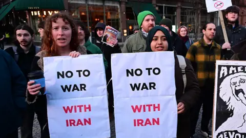 Pacemaker Press A crowd of people are protesting. Two people are holding banners that states no to war with Iran. 