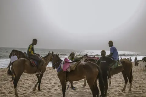 Grace Ekpu/BBC Men on the beach as the sun goes down