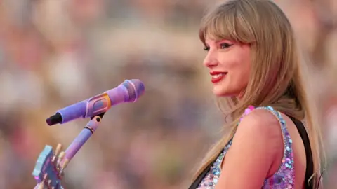 Getty Images Taylor Swift on stage, her side profile is facing the camera and she's smiling with a microphone placed in front of her