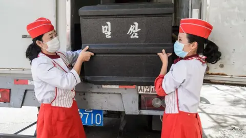 AFP Employees carry a box of wheat cakes stuffed with meat, produced by the Kumsong Foodstuff Factory, to a movable vendor stall in the Central district in Pyongyang