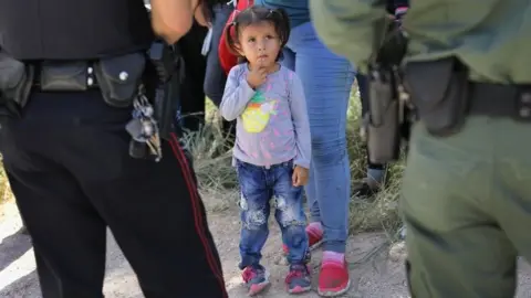 A Mission Police Dept. officer (L) and a US Border Patrol agent watch over a group of Central American asylum seekers before taking them into custody in Texas.