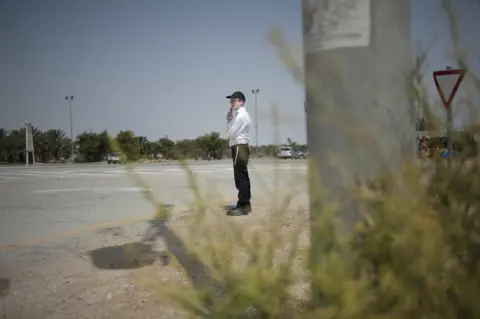 Geraldine Hope Ghelli An Orthodox Jewish man looks out for arriving cars as he waits for the bus at the Nahshon bus junction in Nahson, Israel