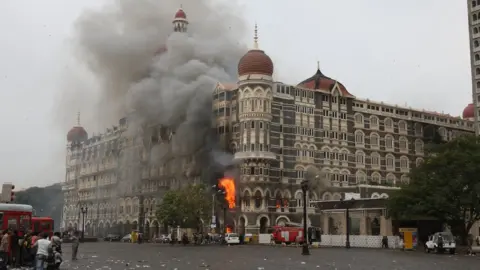 AFP Indian fire brigade officials and bystanders look towards The Taj Mahal hotel in Mumbai on 29 November 2008, as smoke and flames billow out from a section of the building