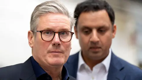 PA Media Sir Keir Starmer, with grey hair and glasses standing in front of Anas Sarwar with black hair.