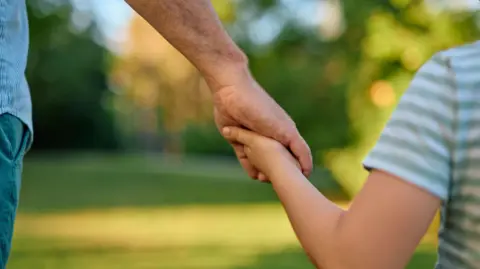 A man holding a child's hand standing in a park 