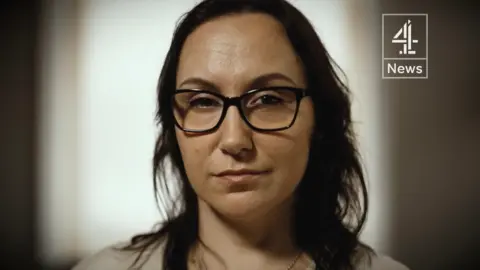 Channel 4 News Joanna faces the camera. She has glasses, dark shoulder-length hair and a light-coloured top.