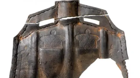 Museum of London Archaeology A brown leather object, with a crown shape embossed into it. It shows signs of age.