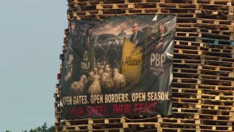 A huge banner depicts small boats, political parties and masked men holding knives