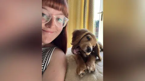 Amber Vellacott A woman and a cute puppy, which is chewing a toy next to her. 