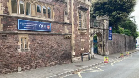 A red brick building with signs says "QEH" on it next to a main road.