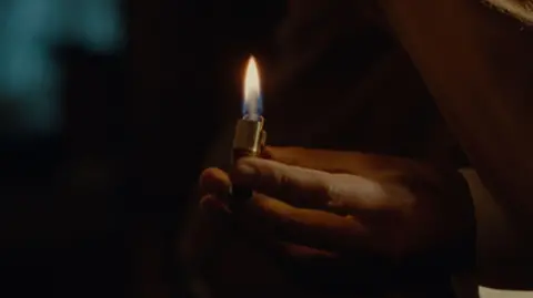 MAB Rabbit Ltd 2024 A hand holding a vintage lighter flipped open, with a lit orange and blue flame.