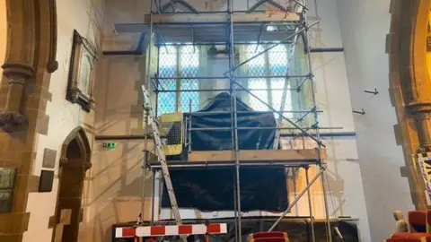 Scaffolding inside St James Church surrounds a stained glass window. 