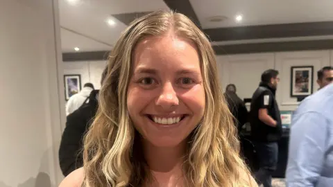 Chloe Rhodes, who has long blonde hair and dark eyes. She is smiling at the camera.