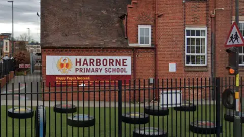 The side of a red brick building with black metal railings and an astroturf area in front, with black discs laid out on it