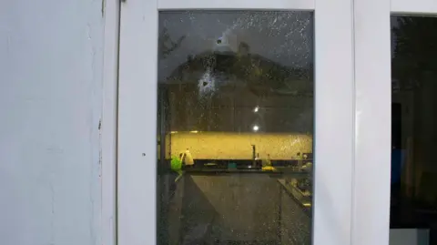 Met Police Two bullets tore through the glass of a conservatory and hit Paul Allen as he stood inside his kitchen. A kitchen light can be seen on in the distance