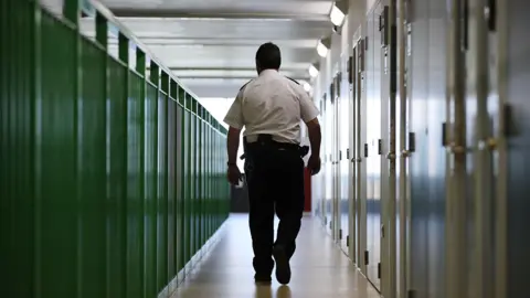A prison guard walks through a cell area at a prison 