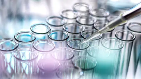 A stock images of a scientist pipetting drop of sample in test tubes in a laboratory. 