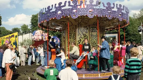 © Keith Haring Foundation/licensed by Artestar, New York. Photo: © Sabina Sarnitz. Courtesy Luna Luna, LLC Children and adults pile onto  Keith Haring’s carousel in Hamburg as others watch on.