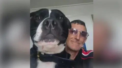 Suffolk Police A close-up photo of a black and white dog's head. Next to it is a man wearing glasses. Both are looking into the camera.
