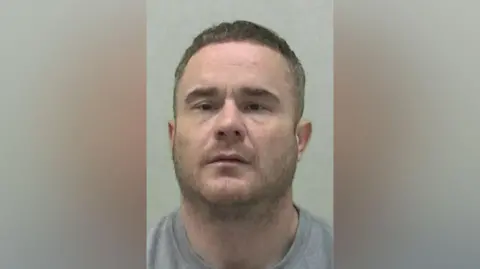 Northumbria Police Mugshot of Ian Black. He has short fair stubble and hair, a thick neck and is wearing a grey t-shirt or sweatshirt. He has relatively small eyes that sit close together.