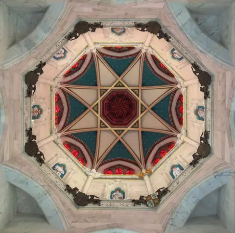 Brian Downie Ceiling of a church, taken from the floor below, showing an octagon style shape with a star shape formed in stained glass, coloured in blue, red, white, and gold