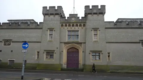 Qays Najm/BBC An exterior shot of County Hall, showing a person walking along the path outside and a one way traffic sign.
