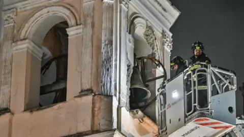 EPA Firefighters in a cherry-picker inspect damage to a church bell tower.