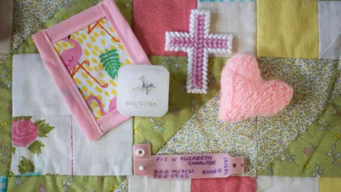 Family handout Family mementos of baby Hazel laid on a quilt including her NHS name tag, a lock of her hair and a small hand knitted pink heart.