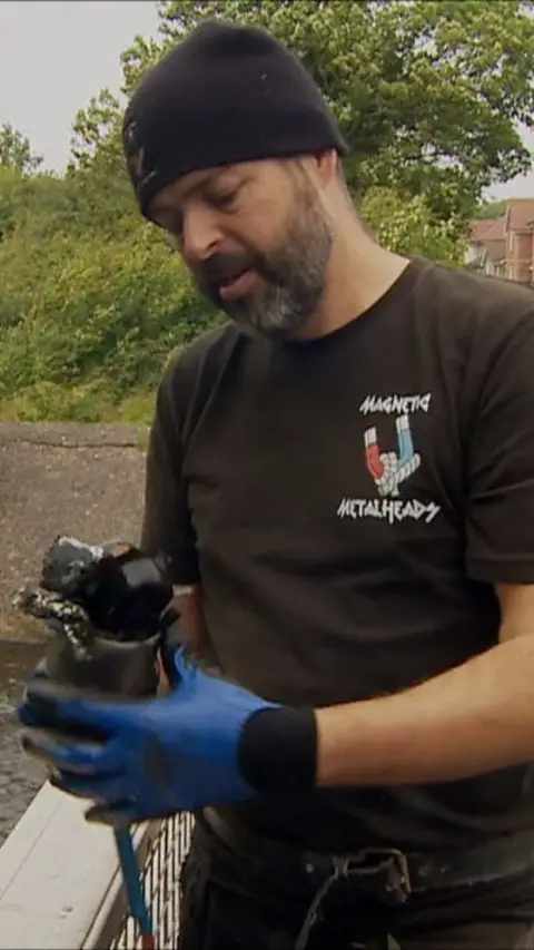 A man wearing a beanie hat and black t-shirt is holding a magnet