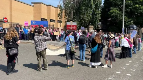 A group of people with placards and banners stand on the pavement and street